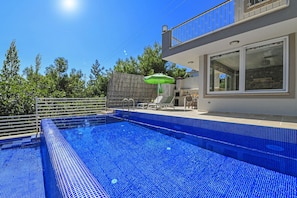 Una piscina al aire libre, sombrillas, sillones reclinables de piscina