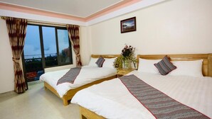 Hotelkamer met twee bedden, een raam met gordijnen, een vaas met bloemen en een lijst met afbeelding.