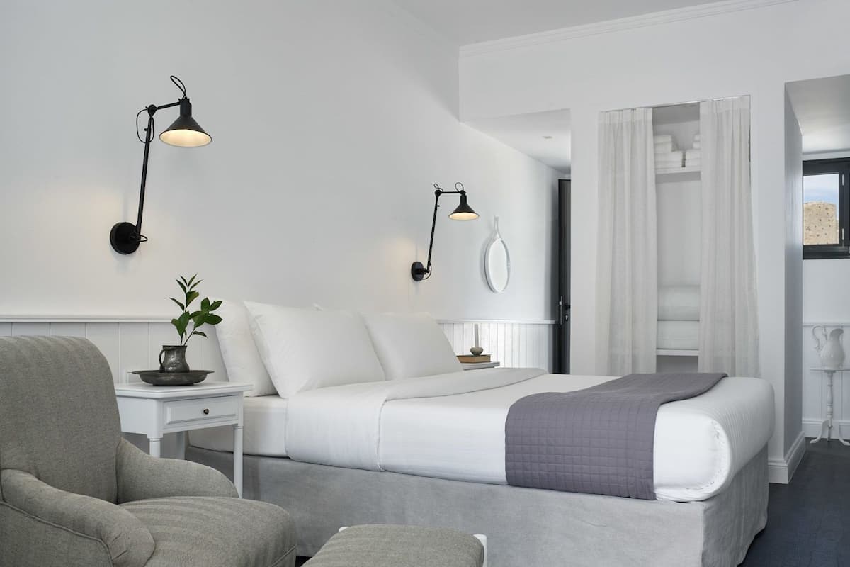 A modern hotel room with a bed, a chair, a bedside table with a lamp, and a plant.