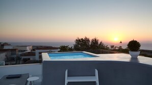 Una piscina en la azotea con vistas a la puesta de sol sobre el mar, rodeada de edificios.