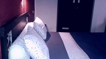A hotel room with a bed, pillows, a remote control, and a minibar.