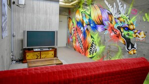 Una habitación con un televisor grande, un sofá rojo y un mural colorido en la pared.