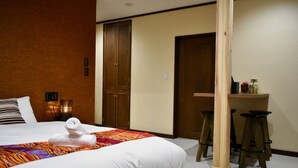Habitación de hotel con una cama grande, un armario de madera, una pequeña zona de bar con taburetes y una puerta que da a otra habitación.