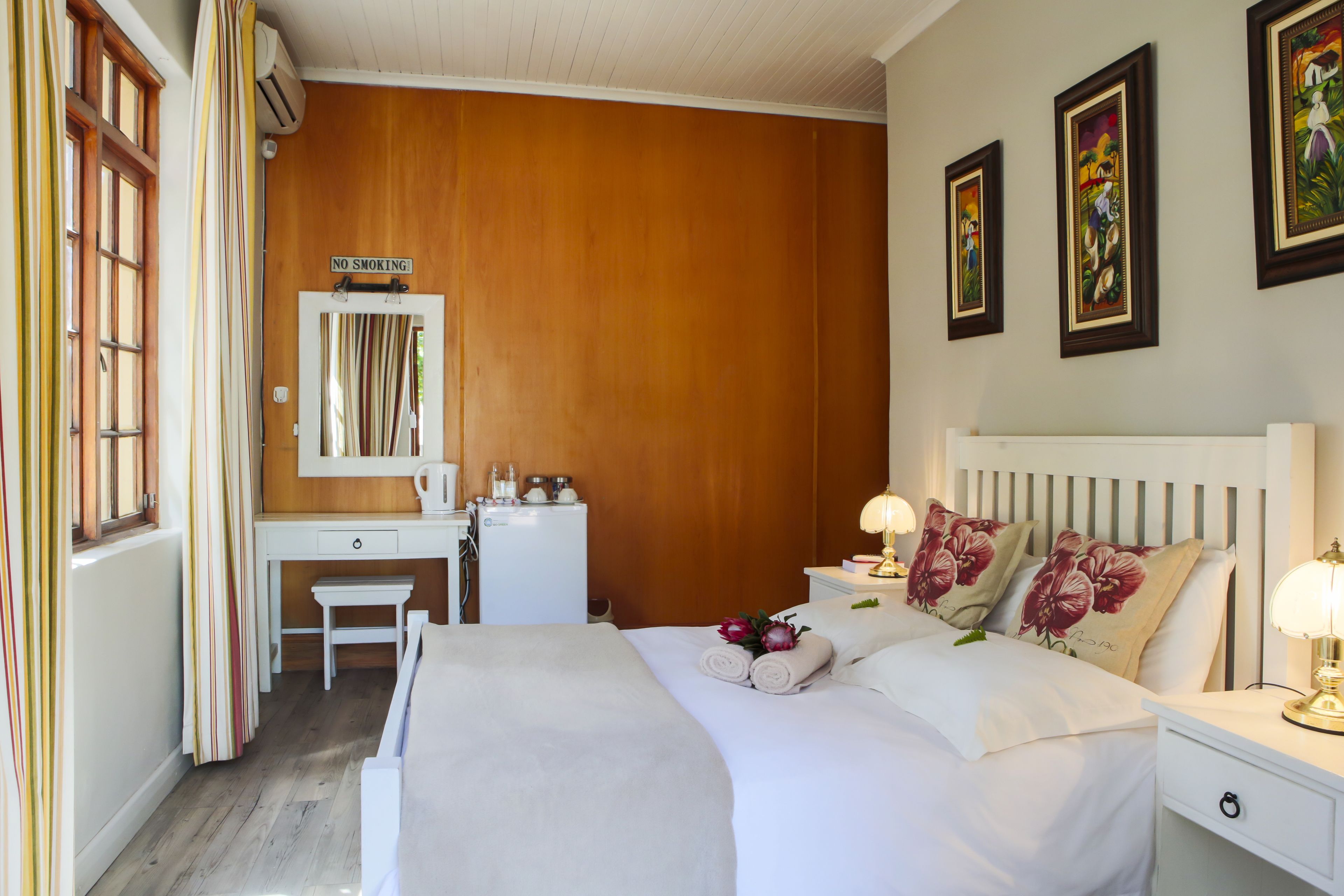 A hotel room with a bed, bedside table, lamp, and a small desk with a chair.