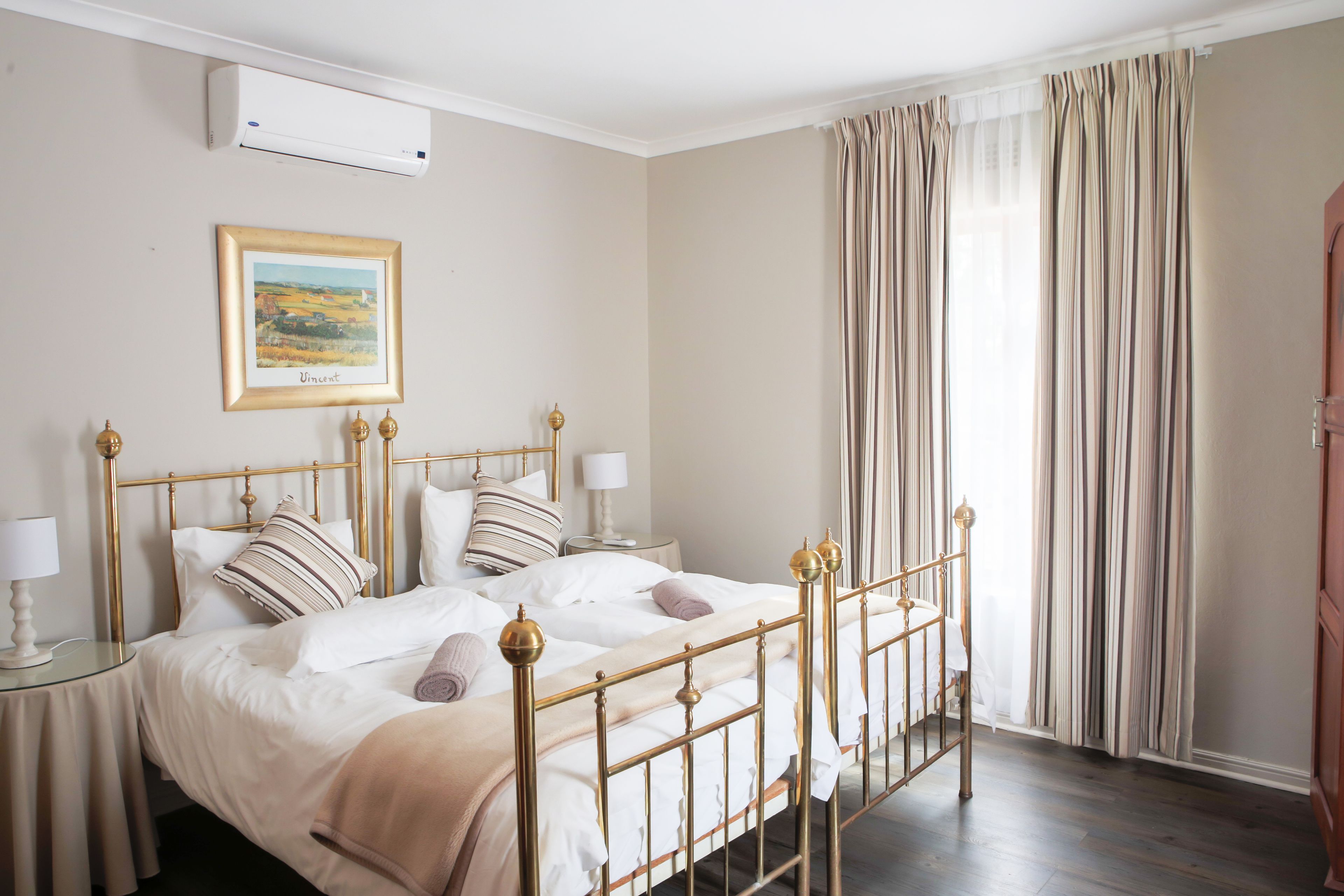 A bedroom with a bed, bedside tables, a lamp, a framed picture on the wall, and a window with curtains.