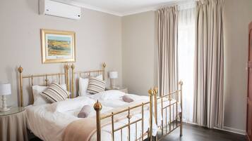 Un dormitorio con cama, mesitas de noche, lámpara, un cuadro enmarcado en la pared y ventana con cortinas.