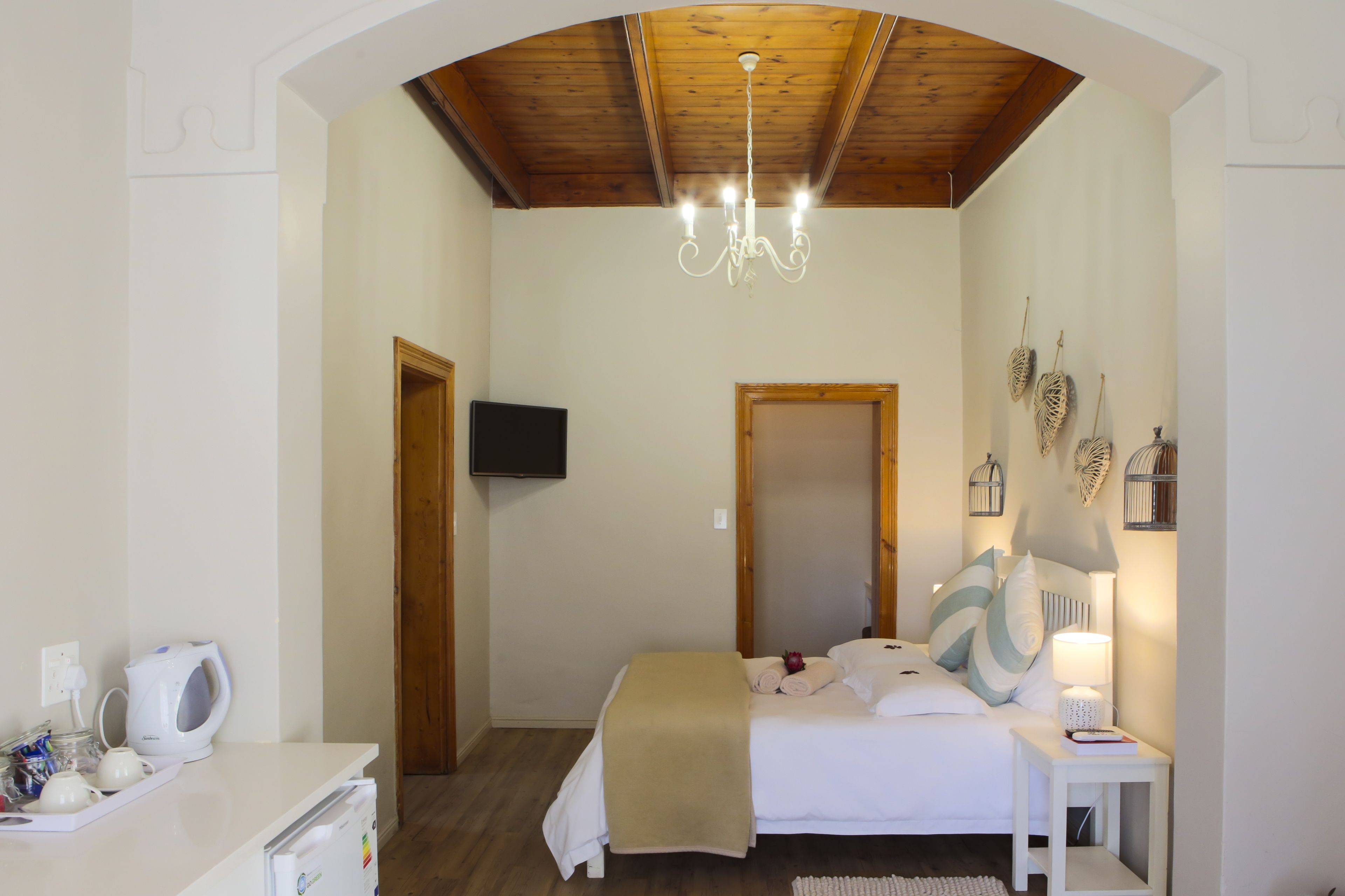 Een slaapkamer met een houten plafond, een bed met wit beddengoed, een nachtkastje met een lamp, en een aan de muur bevestigde televisie.