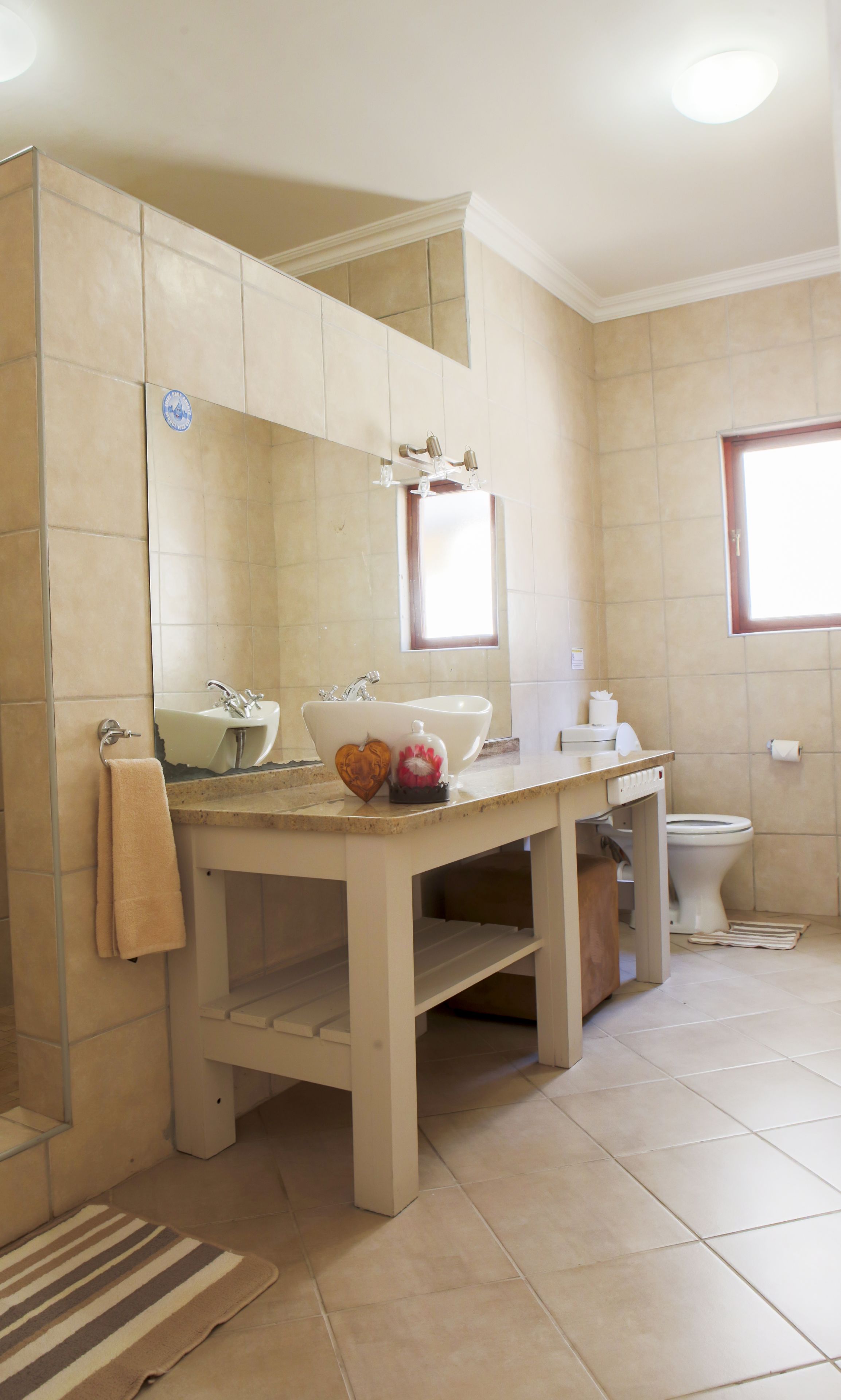 A bathroom with a large mirror, two sinks, a toilet, and a window.