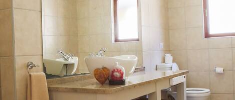 A bathroom with a large mirror, two sinks, a toilet, and a window.