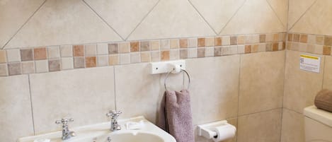 Un baño con lavamanos pedestal, tapa de inodoro de madera y espejo sobre el lavamanos.