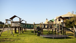 Ein Spielplatz mit einer Holzkonstruktion, einem Trampolin und einem grünen Kletternetz.
