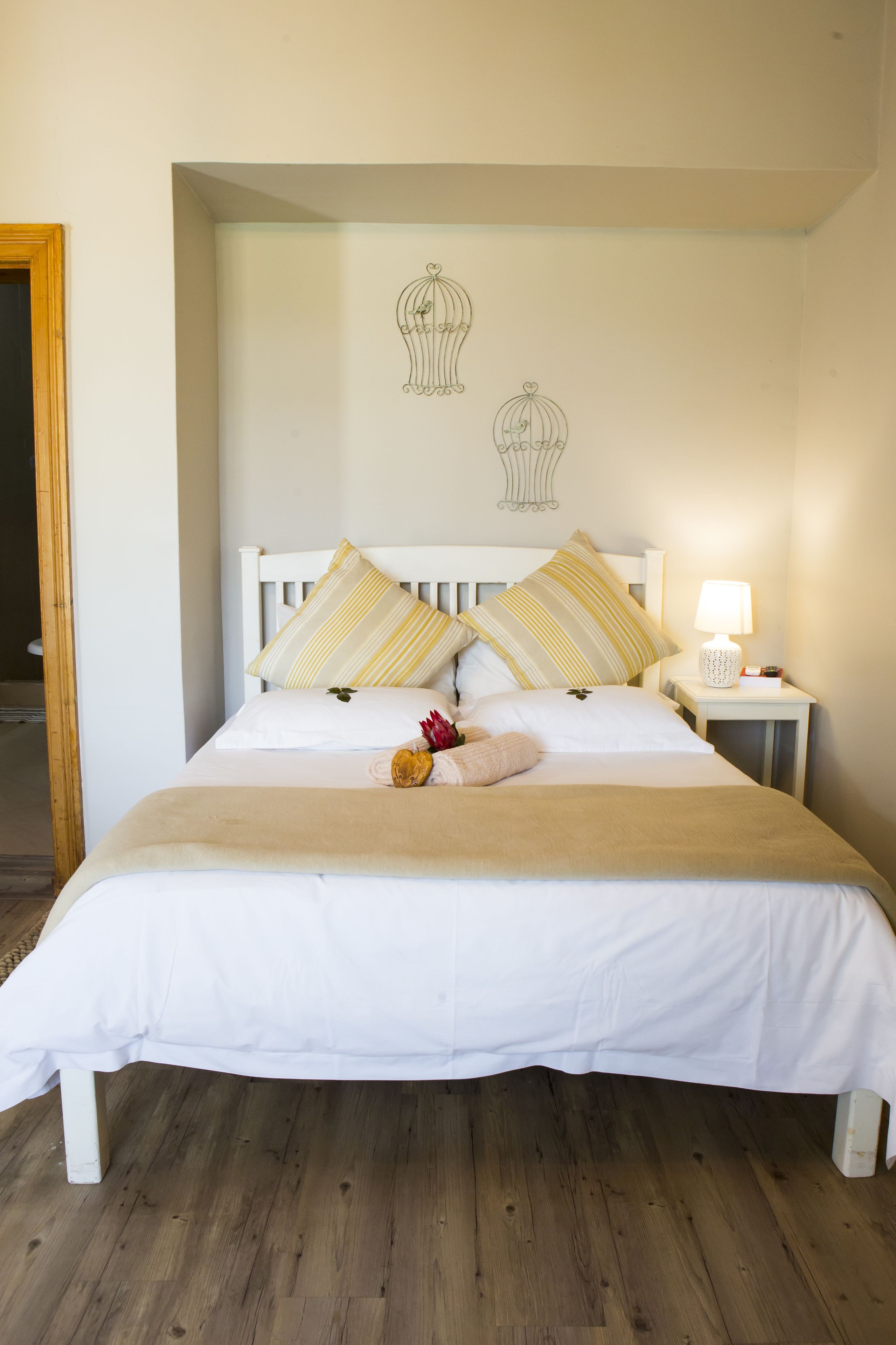 Een netjes opgemaakt bed met witte beddengoed en gestreepte kussens, een bedlampje en een muur met vogelafbeeldingen.