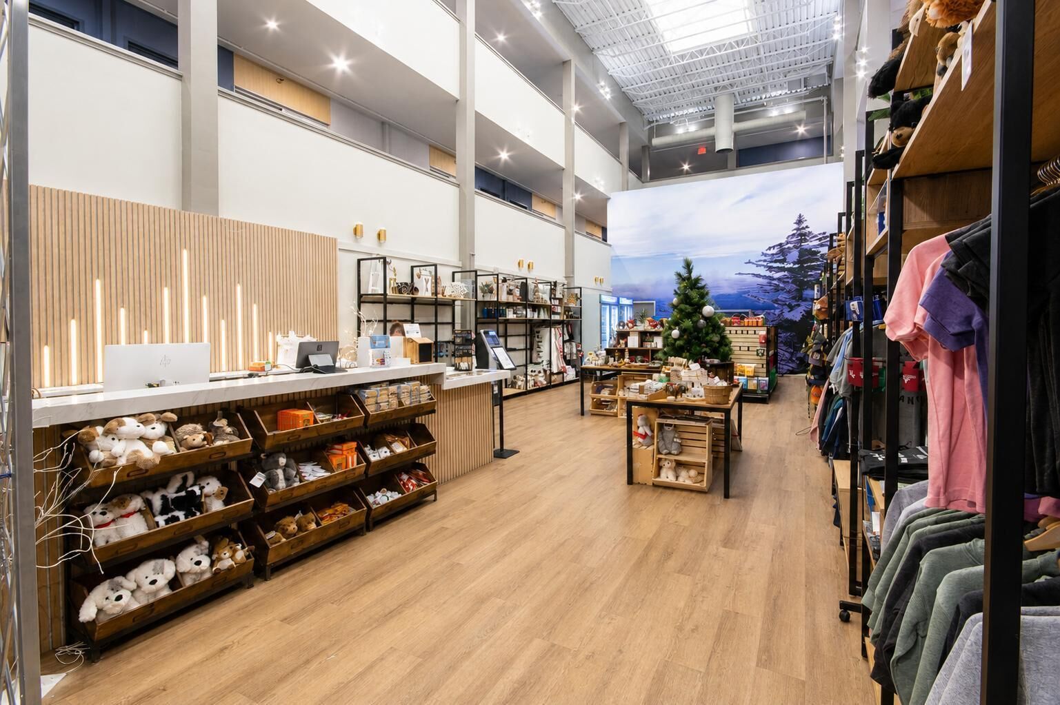A spacious retail store with wooden flooring, shelves stocked with various items, a Christmas tree, and a checkout counter.