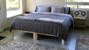 Ein Schlafzimmer mit einem Bett, zwei Nachttischen, einem Deckenventilator und großen Fenstern.