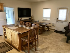 A kitchen with a wooden island, dining table, chairs, and a TV mounted on the wall.