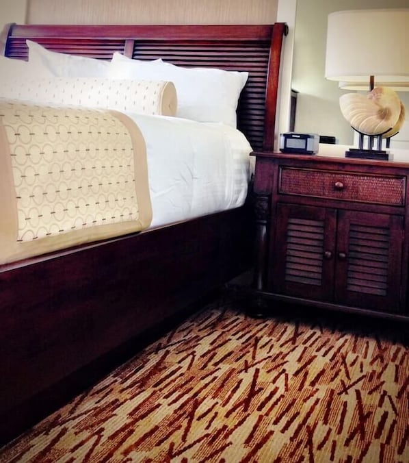 A neatly made bed with a patterned bedspread and pillows, a wooden nightstand with a lamp, and a patterned carpet.