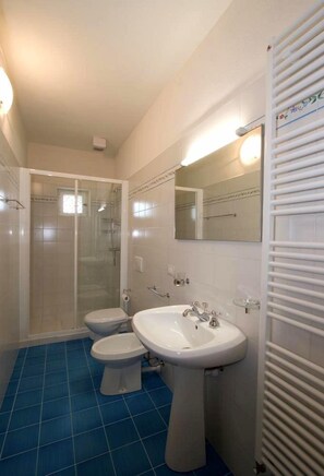 Une salle de bain avec une douche, deux toilettes, un lavabo et un miroir.