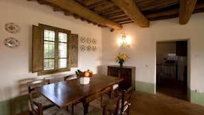 Une salle à manger avec une table en bois, des chaises, un vase de fleurs et une fenêtre avec des rideaux.