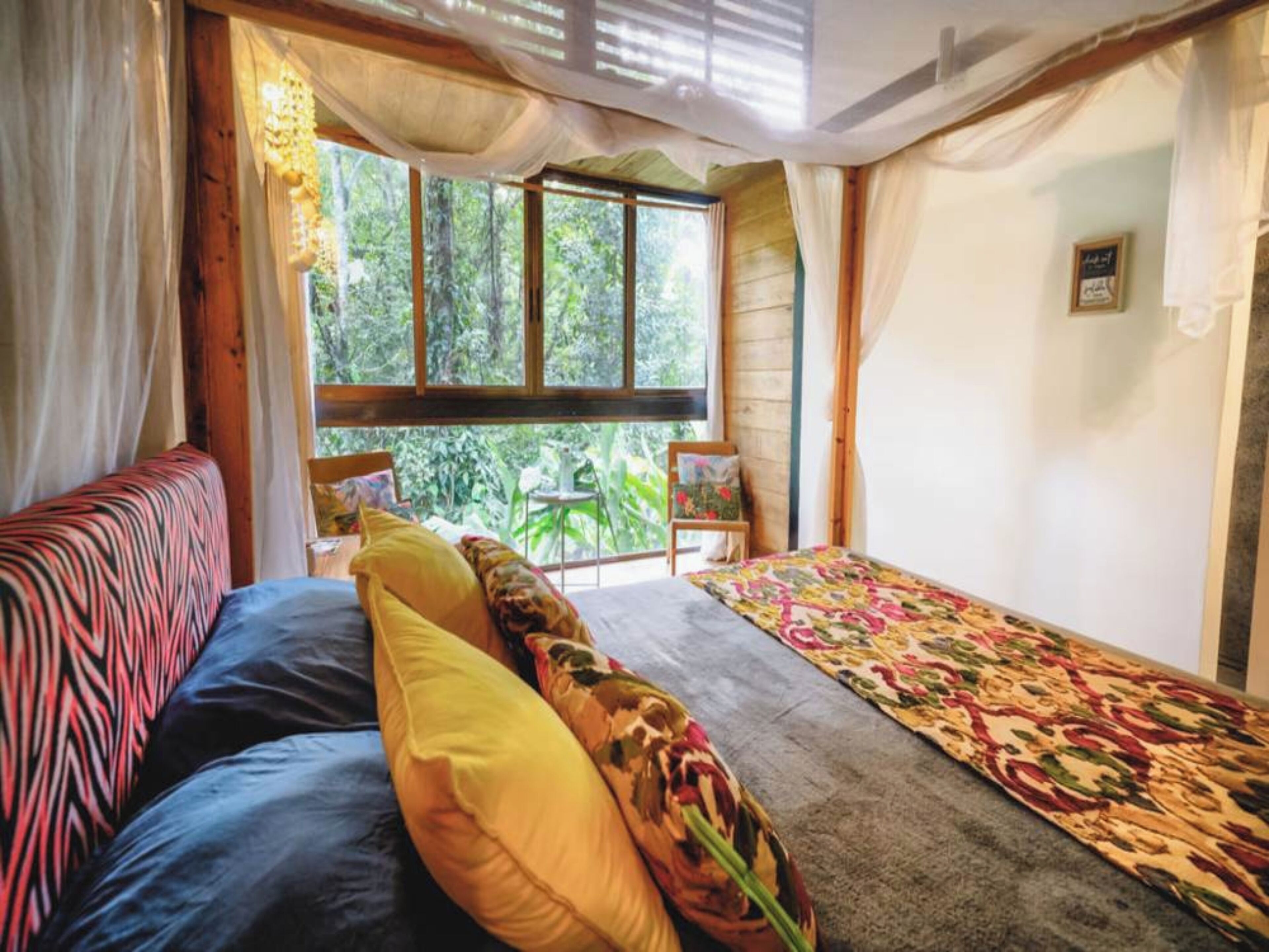 A cozy bedroom with a bed, a sofa, and a window overlooking greenery.