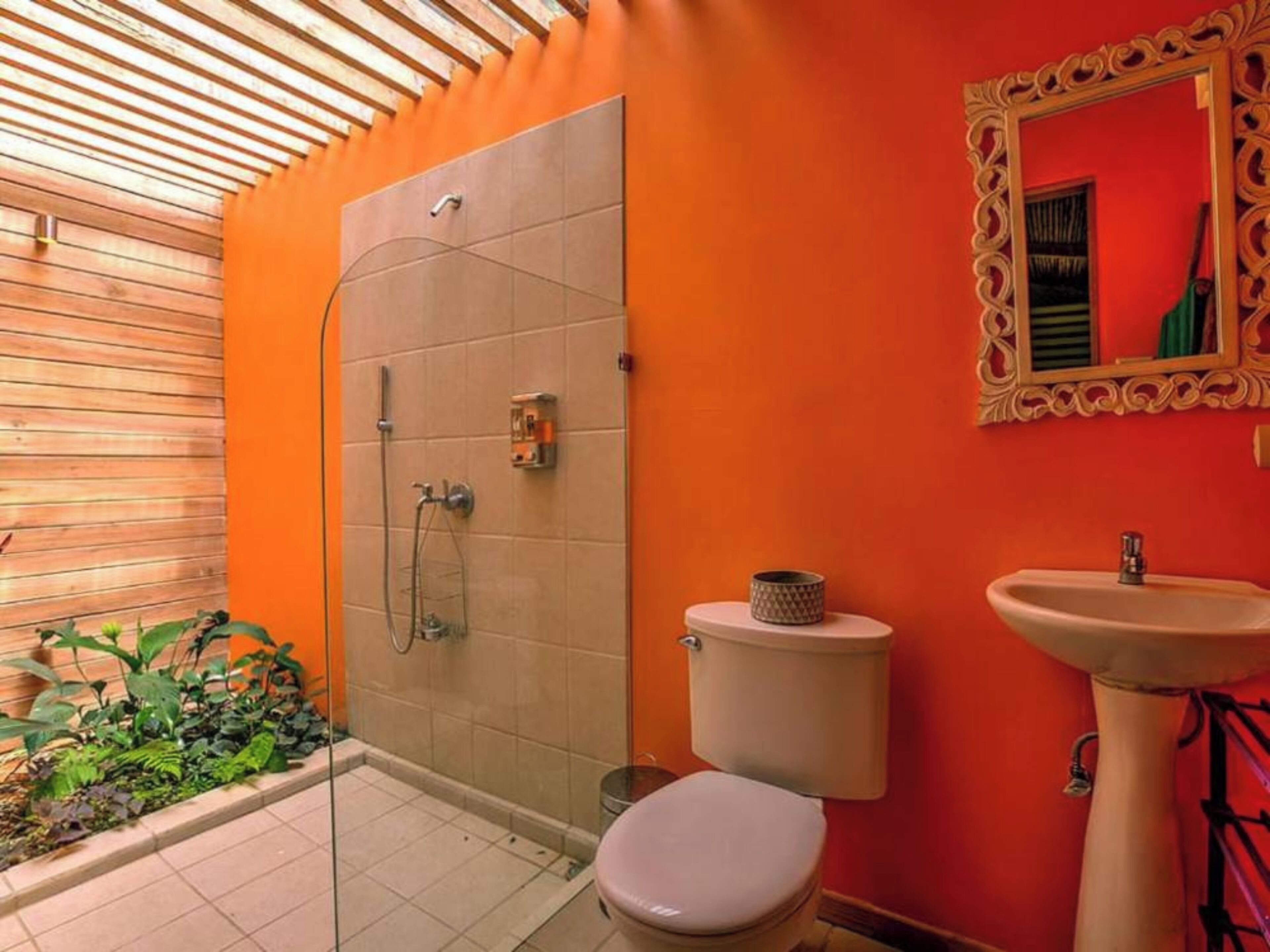 A bathroom with a shower, toilet, and sink, featuring orange walls and wooden ceiling beams.