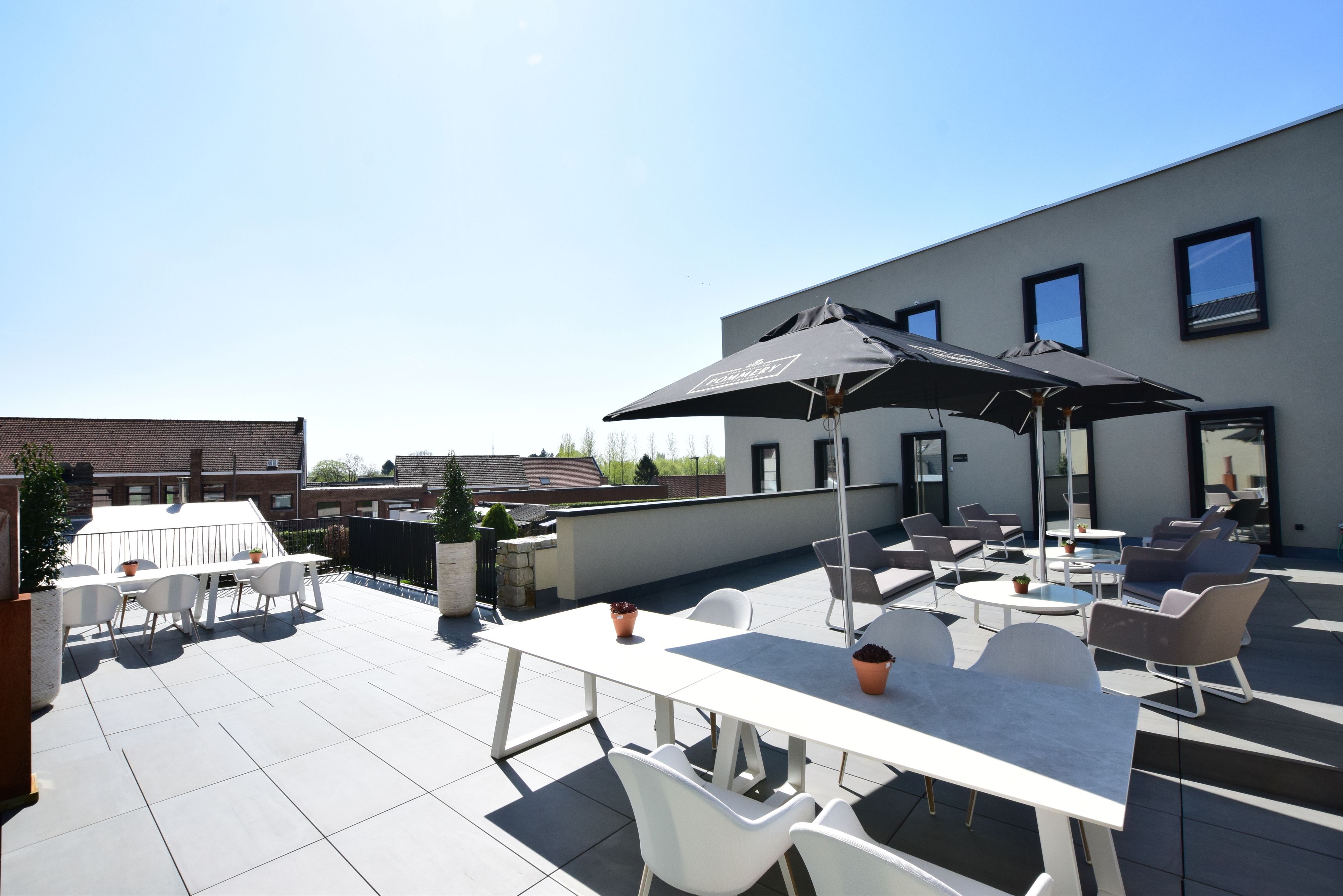 A rooftop terrace with a table and chairs, a large umbrella, and a modern building in the background.