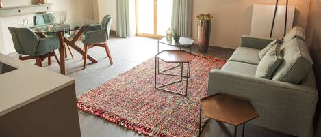Una sala de estar moderna con una mesa de comedor de vidrio, sillas verdes, un sofá gris y una alfombra estampada.