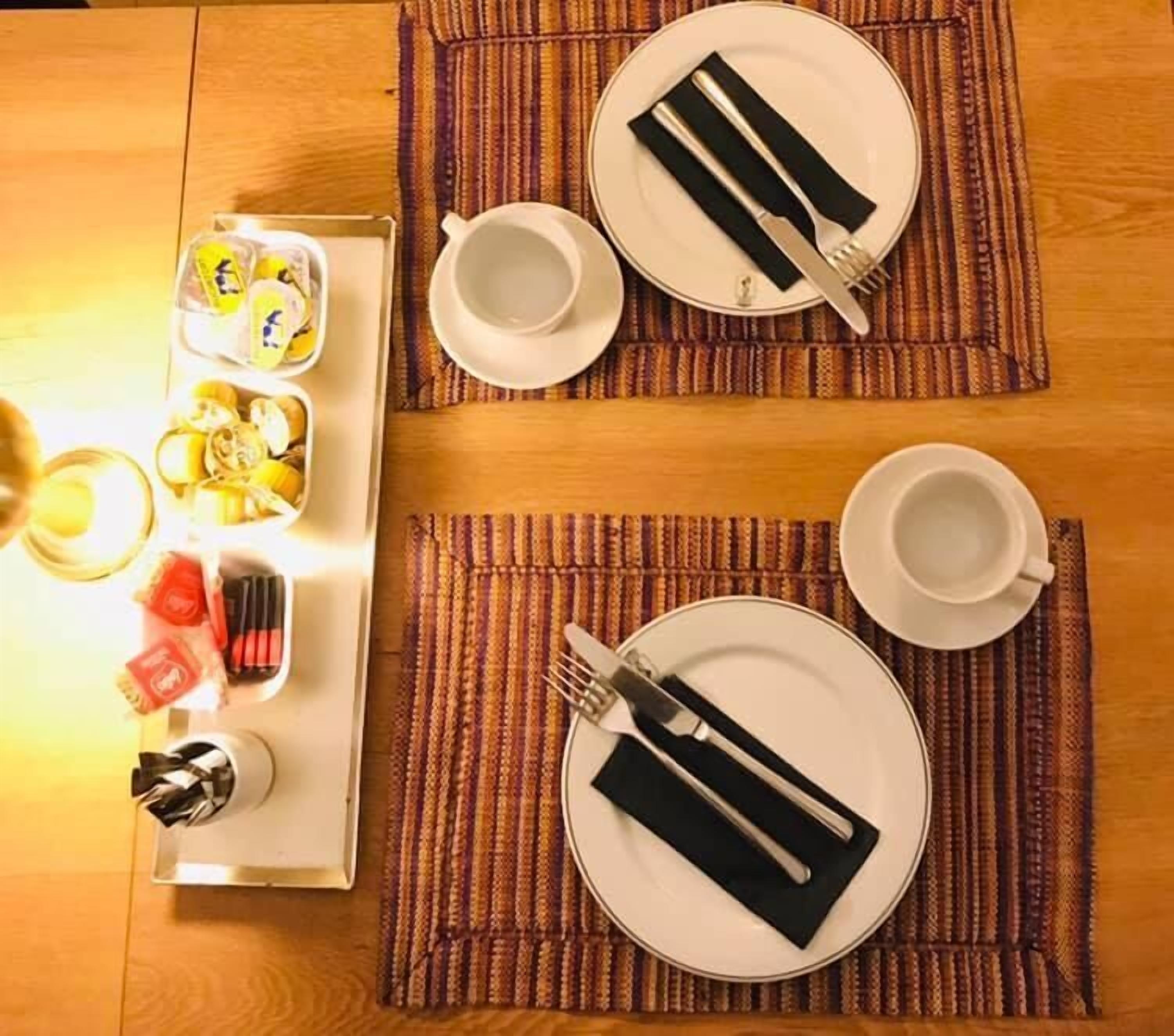 A dining setup with two plates, cutlery, and a tray of food items on a wooden table.