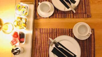 A dining setup with two plates, cutlery, and a tray of food items on a wooden table.