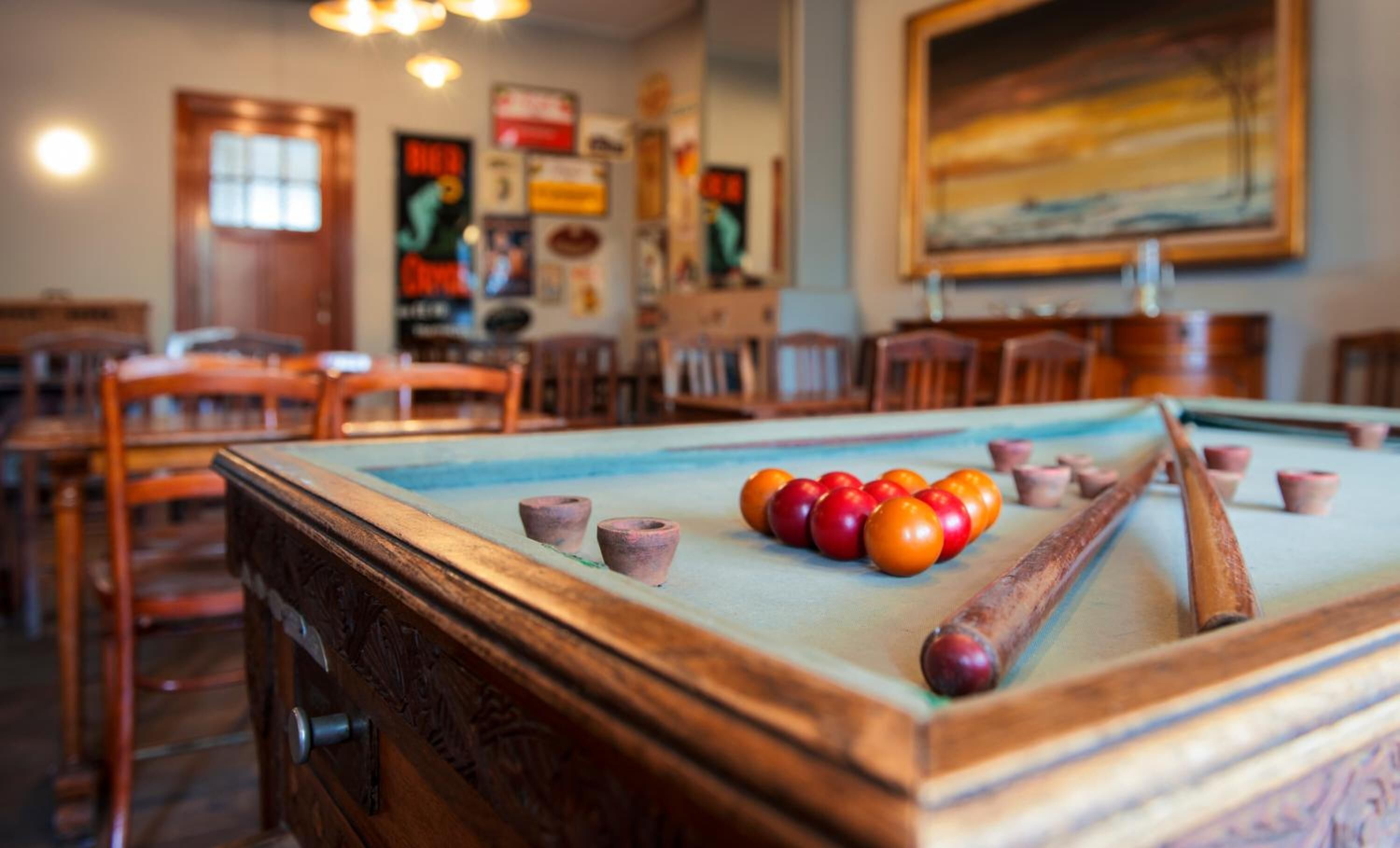 A pool table with balls, wooden chairs, and a painting on the wall.