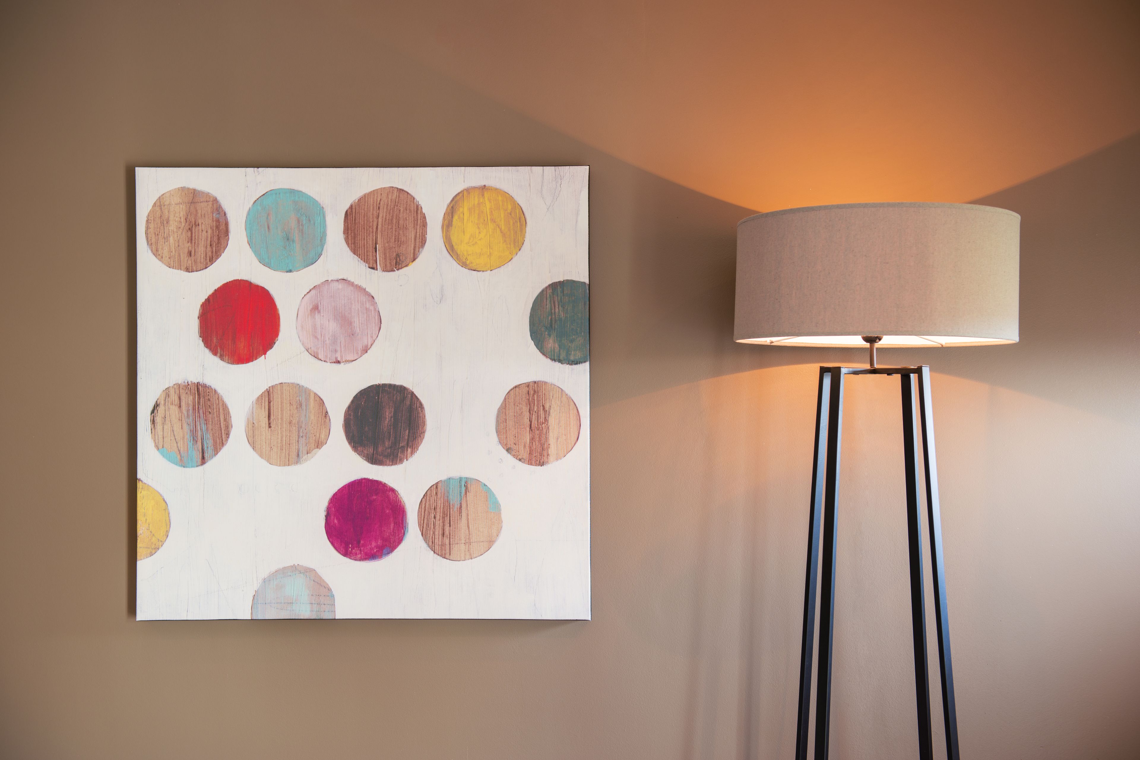 A wall-mounted painting with various colored circles and a floor lamp with a cylindrical shade.