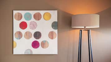 A wall-mounted painting with various colored circles and a floor lamp with a cylindrical shade.