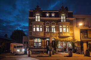 Un edificio histórico con amplios vitrales, un balcón y una camioneta antigua estacionada frente a él.