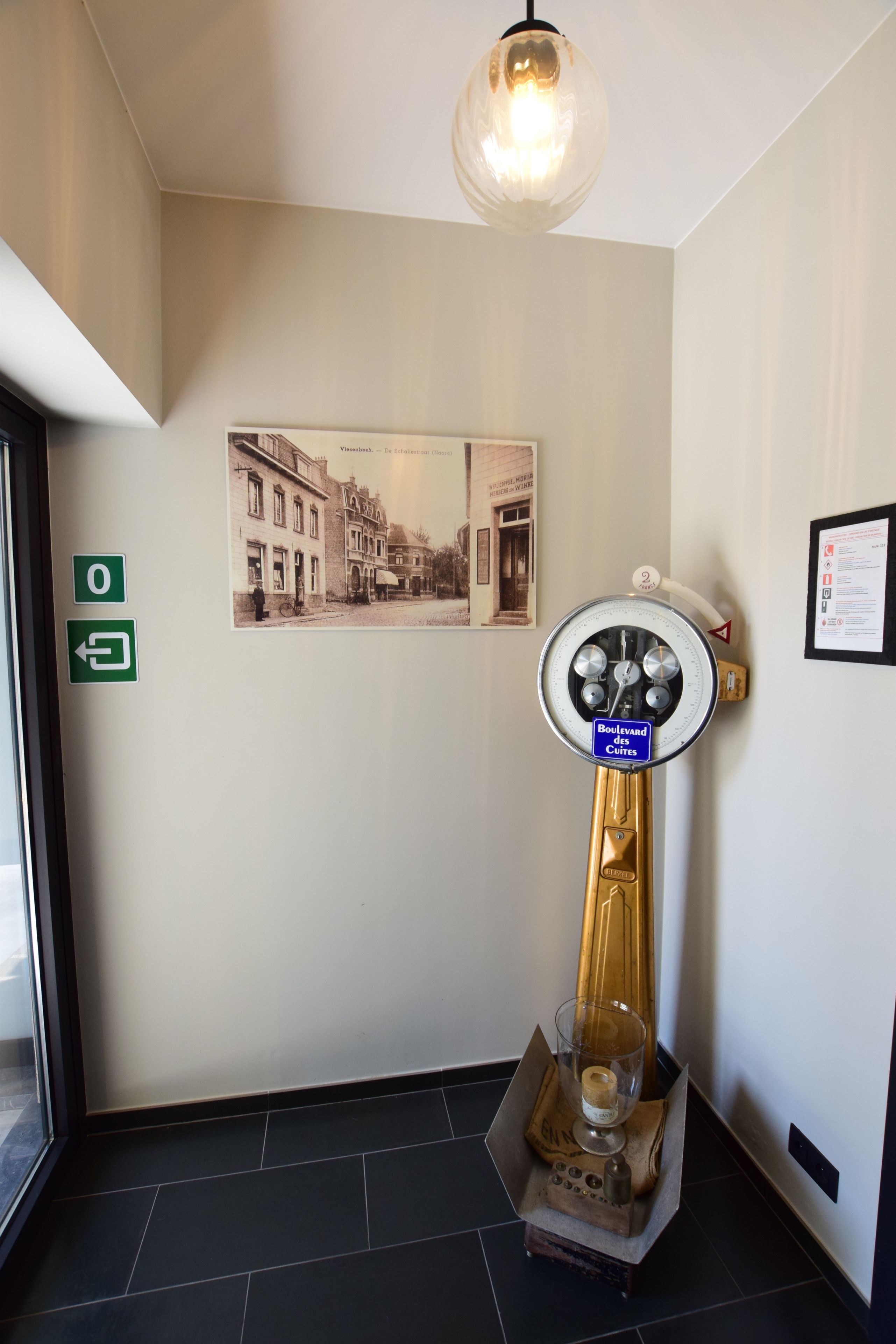 Un vestíbulo con un teléfono rotatorio antiguo, un vaso de agua y una fotografía enmarcada en la pared.