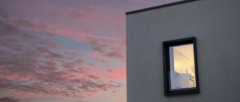 A building with a window reflecting a sunset sky.