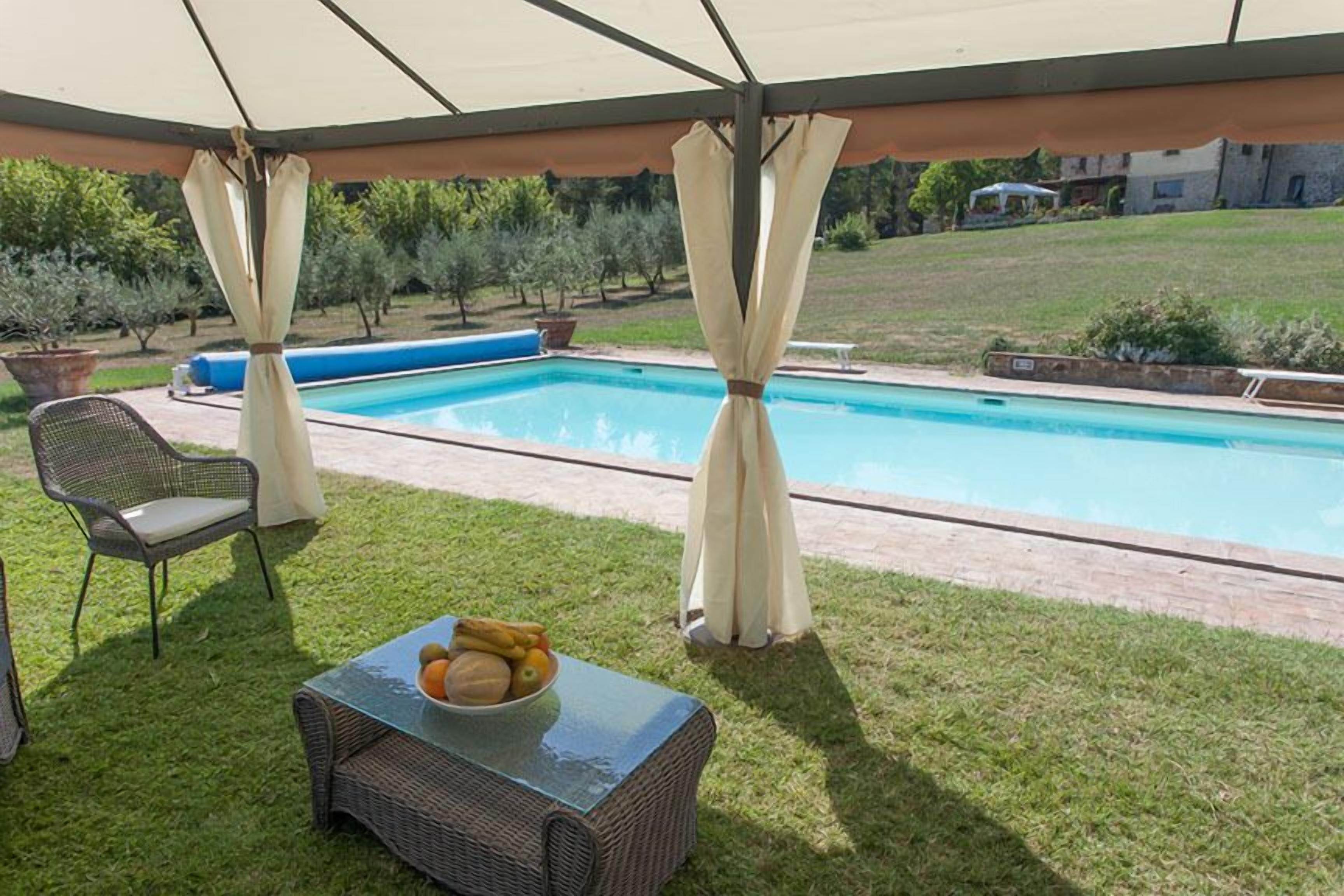 Een overdekt terras met een zwembad, rieten meubels en een tafel met fruit.