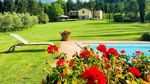 A pool area with a lounge chair, a flower bed with red flowers, and a house in the background. - Verdidea - Villa la Felce (Cetona)