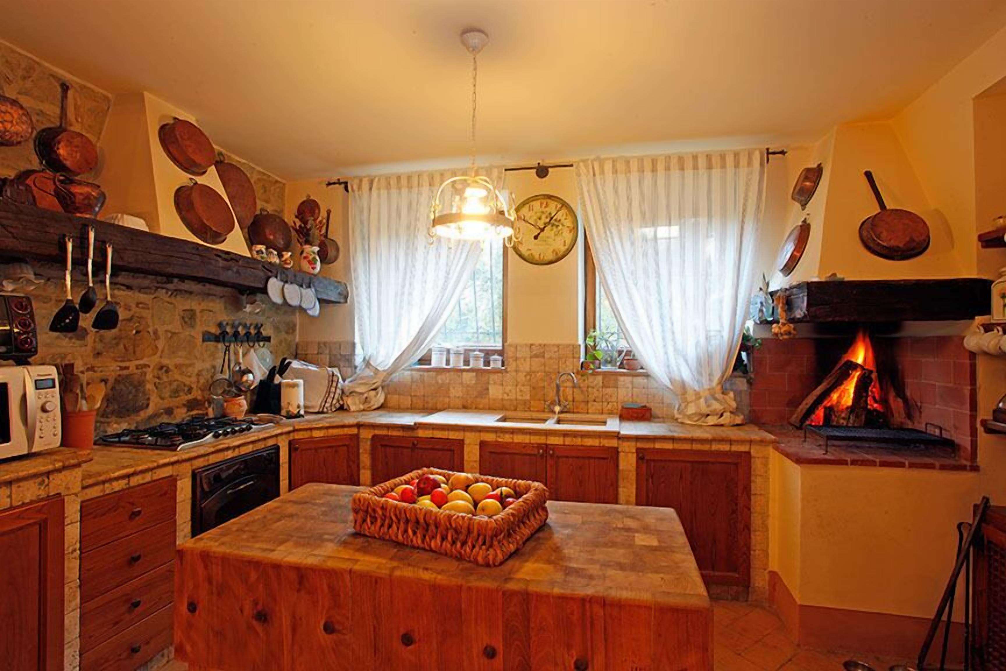 A rustic kitchen with a stone wall, wooden cabinets, a built-in oven, and a fruit basket on the island.