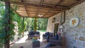 A covered outdoor seating area with wicker furniture, stone walls, and a view of greenery. - Verdidea - Villa la Felce (Cetona)