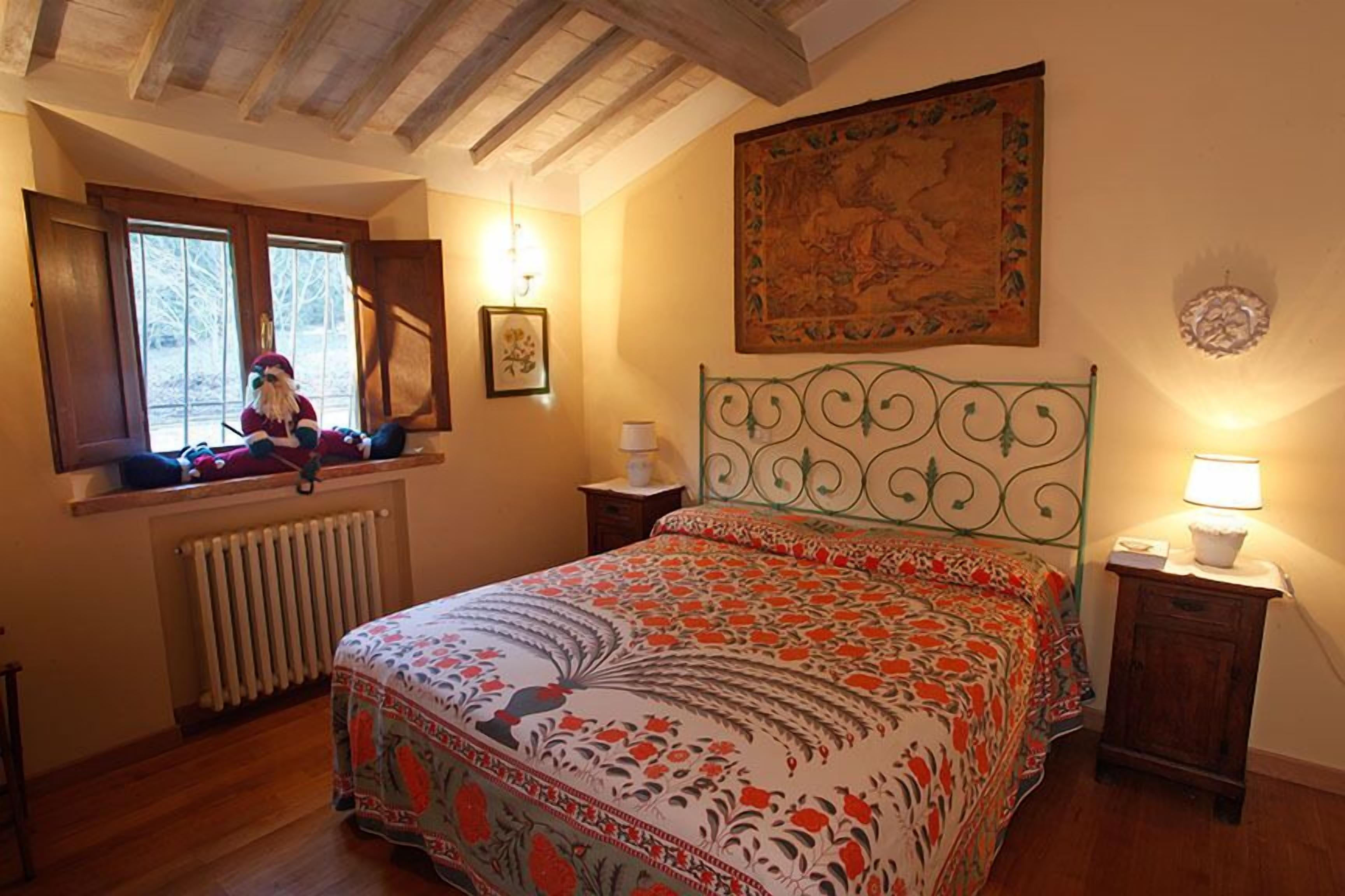 Un dormitorio con cama, ventana con vistas, radiador, techo de madera y una lámpara de pared.
