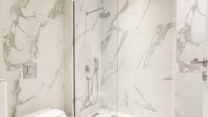 Une salle de bain moderne avec une douche à parois de verre, des murs en marbre et des toilettes blanches.