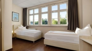 Een hotelkamer met twee enkele bedden, een groot raam met gordijnen, een lijst met afbeelding aan de muur en een houten vloer.