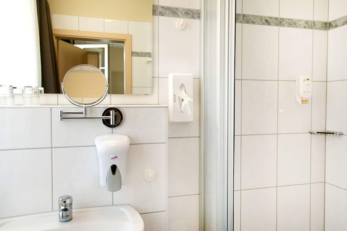 A bathroom with a white sink, a mirror, a soap dispenser, and a towel dispenser.