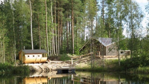 Une cabane avec un quai s’avançant dans un lac, entourée de grands arbres.