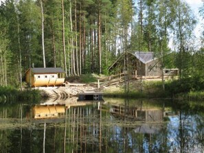 Une cabane avec un quai s’avançant dans un lac, entourée de grands arbres.