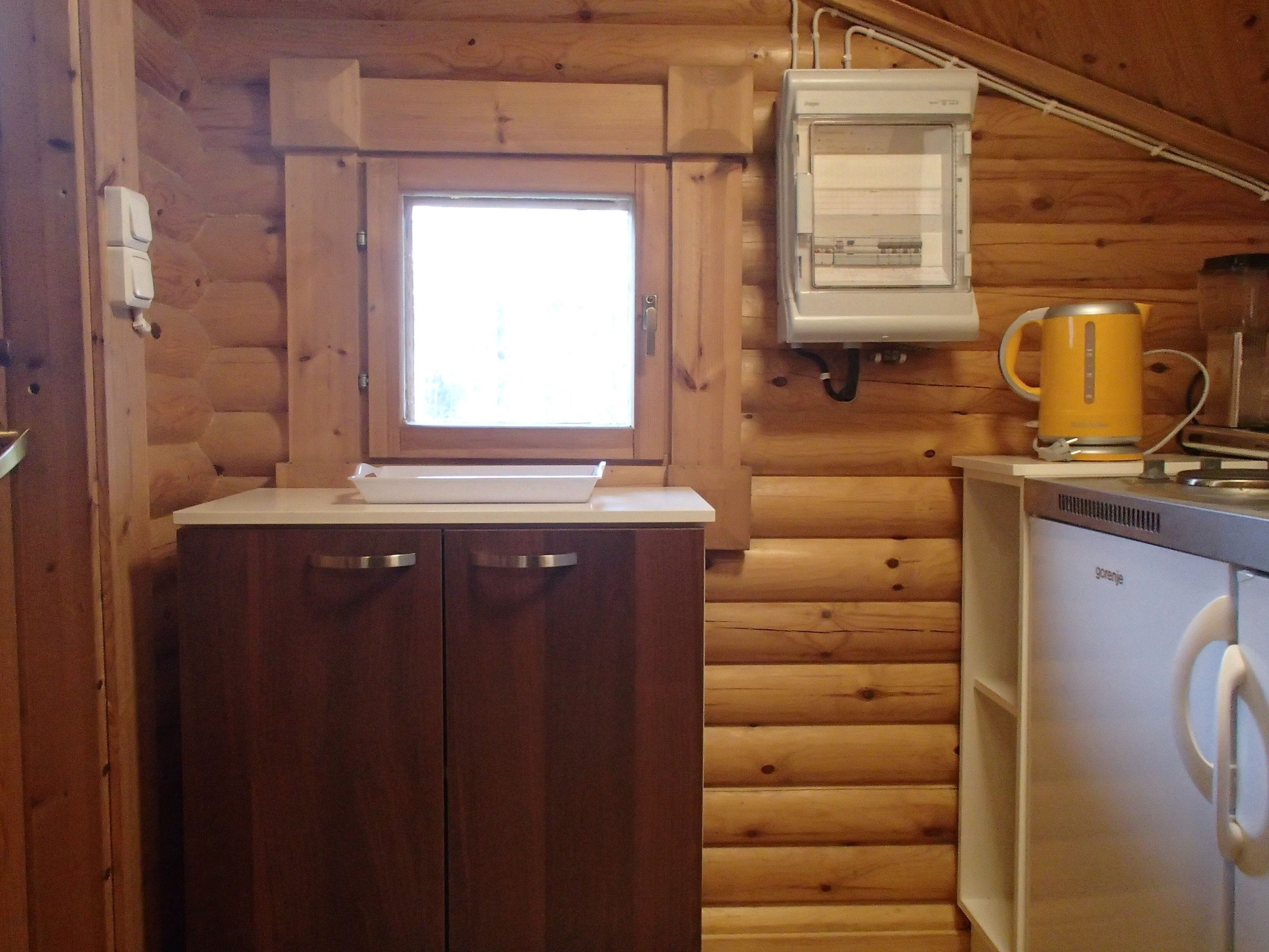 Una cocina compacta con paredes de madera, una encimera blanca, un horno empotrado y un hervidor amarillo.