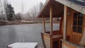 Une cabane en bois avec un quai s’avançant sur un lac gelé, le tout entouré d’arbres.