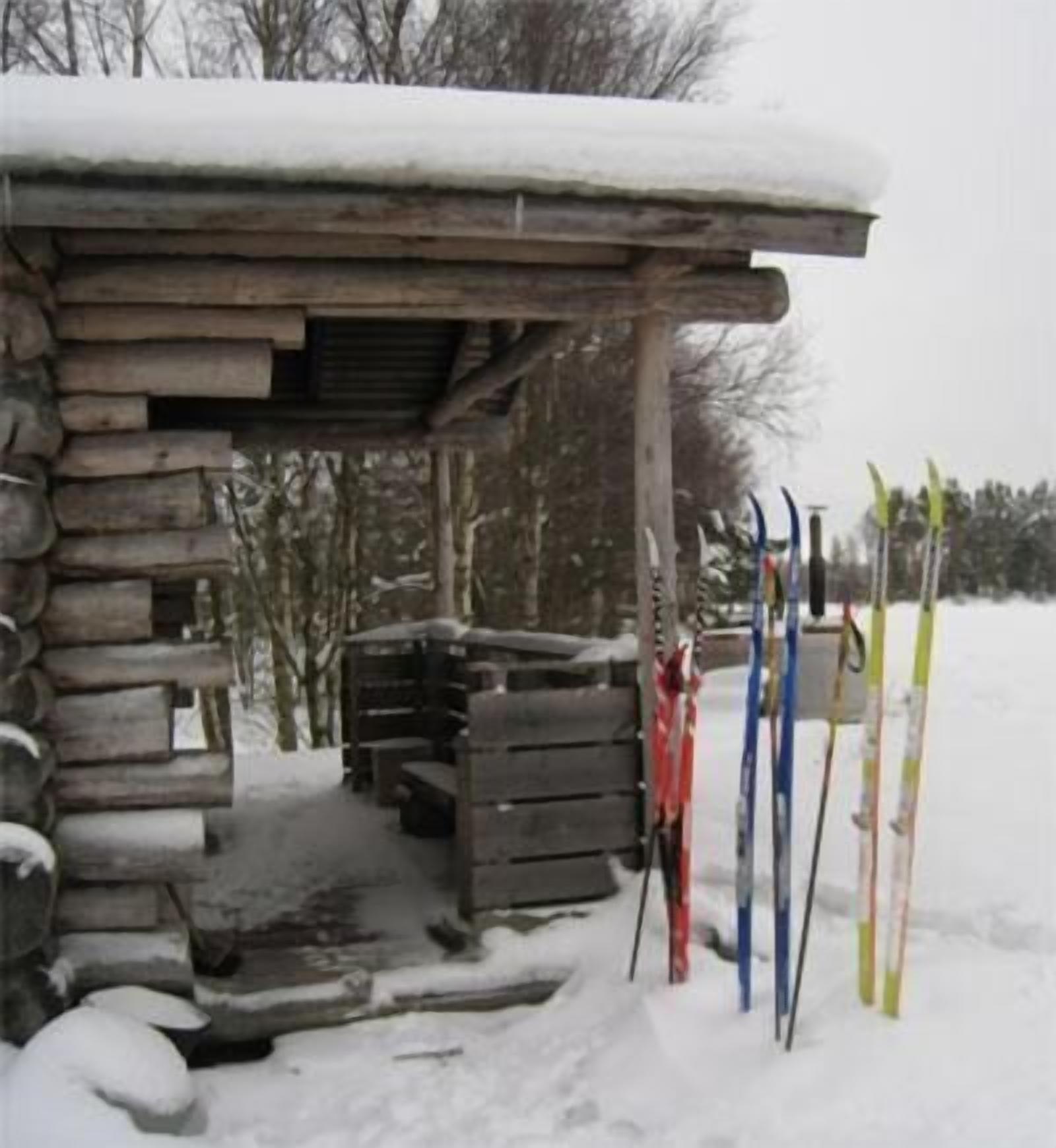 A rustic wooden cabin with a snow-covered roof and a wooden staircase leading up to a door.