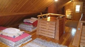 Une chambre mansardée chaleureuse avec des murs en bois et un plafond en pente. On y trouve deux lits avec des oreillers et des couvertures, un berceau en bois et une petite table.