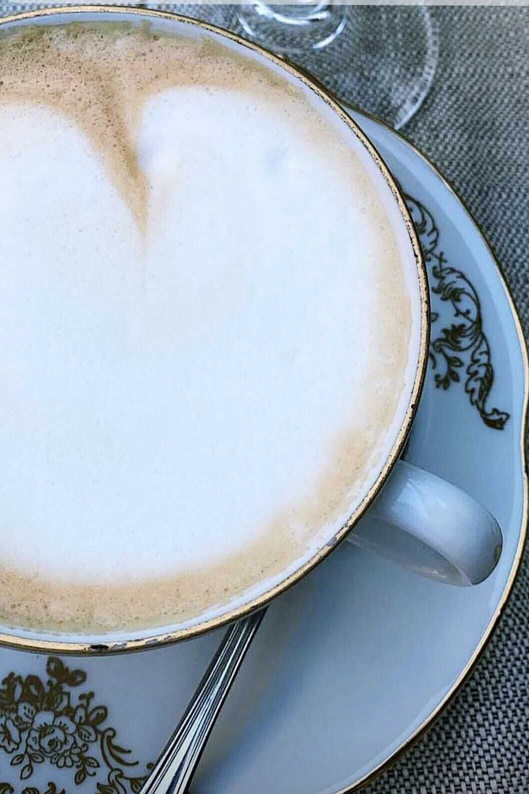 A cup of coffee with a creamy foam top, placed on a saucer with a floral pattern.