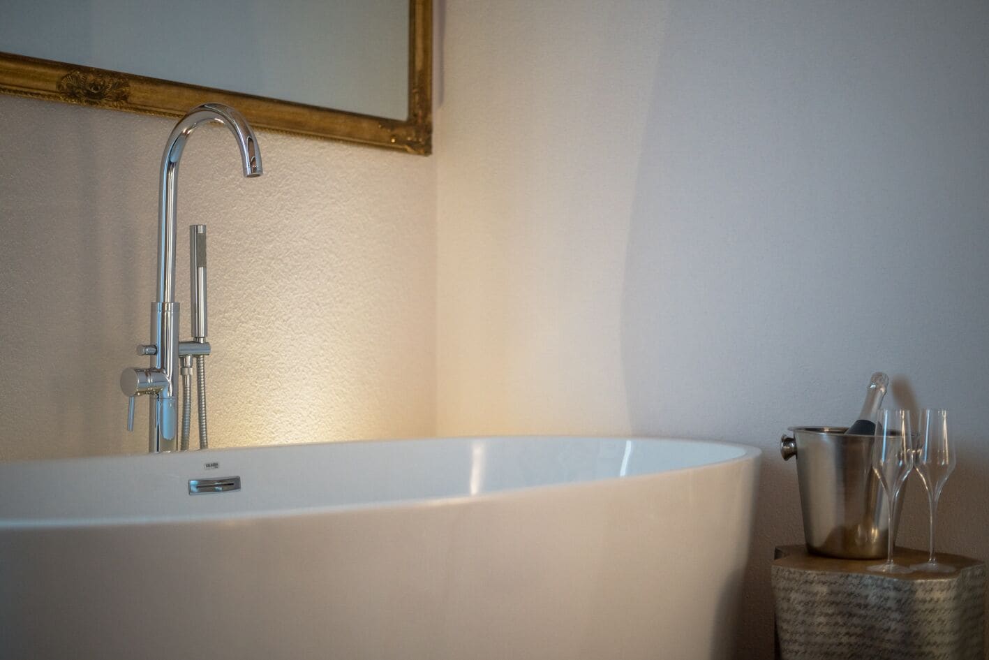 A modern bathroom with a freestanding bathtub, a handheld showerhead, and a small side table with a champagne bottle and glasses.